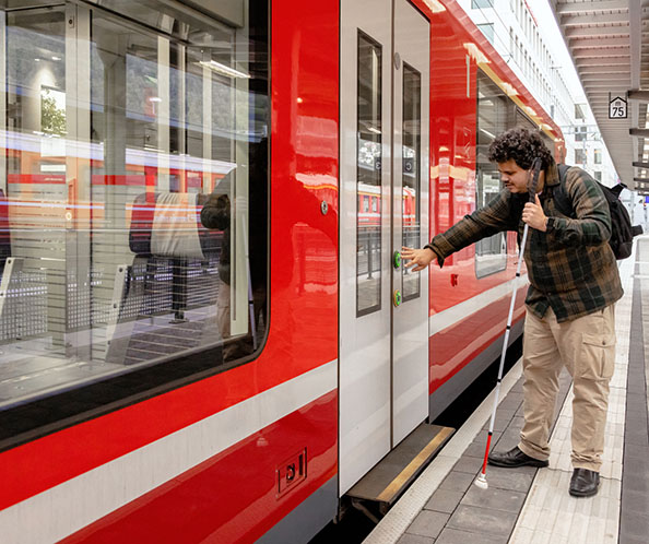 Un homme avec une canne blanche appuie sur le bouton d’ouverture des portes d’un train.