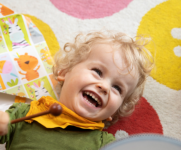 blonder, zweieinhalb jähriger Junge lachend auf Spieldecke