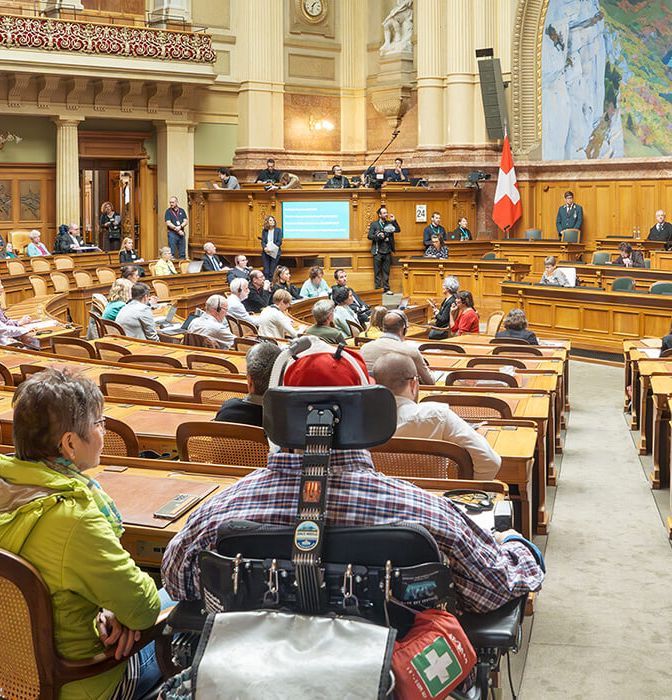 Teilnehmende der Behindertensession 2023 auf den Parlamentsplätzen im Nationalratssaal, darunter Personen im Rollstuhl.