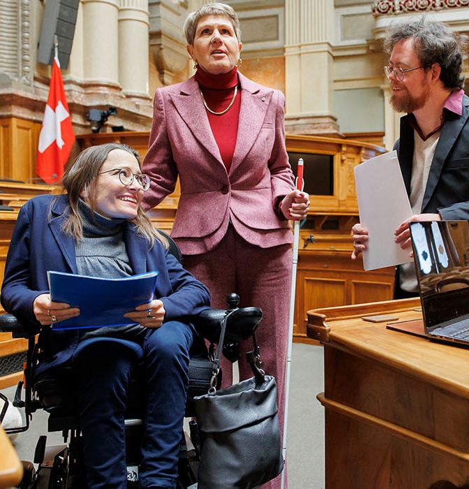 Drei Menschen mit Behinderungen im Nationalratssaal des Bundeshauses