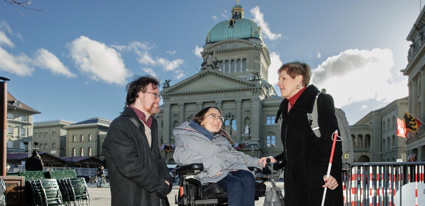 Trois personnes en situation de handicap devant le Palais fédéral