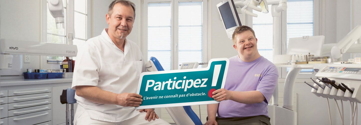 Un dentiste et un patient ayant le syndrome de Down tiennent une pancarte sur laquelle est écrit : « Participez ! L’avenir ne connaît pas d’obstacle. »