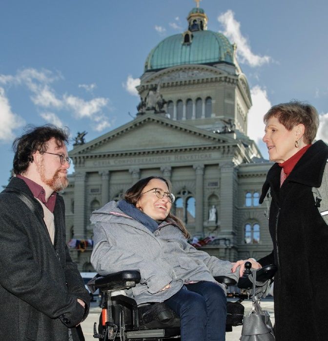 Trois personnes en situation de handicap devant le Palais fédéral