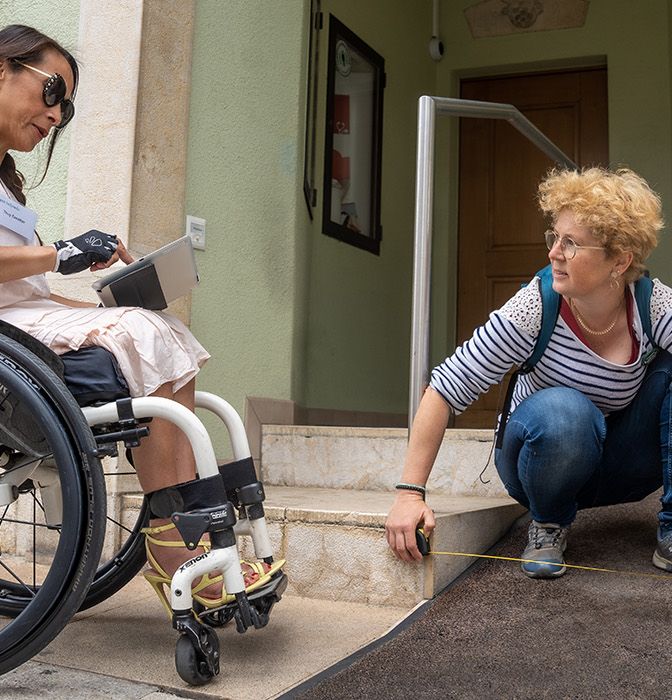 Deux personnes (dont une en fauteuil roulant) mesurent l'entrée d'un bâtiment