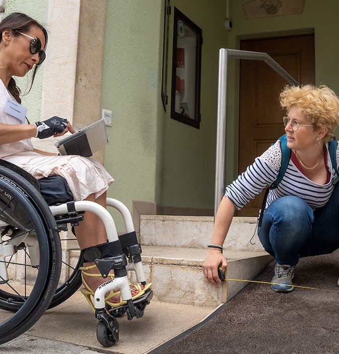 Due persone (una in sedia a rotelle) misurano l'ingresso di un edificio