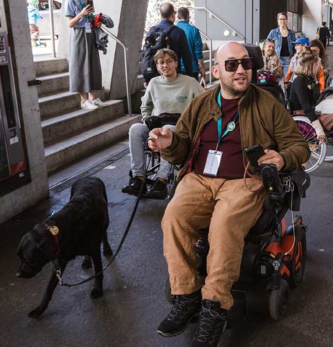 Personen in Rollstühlen auf einem Bahnsteig.