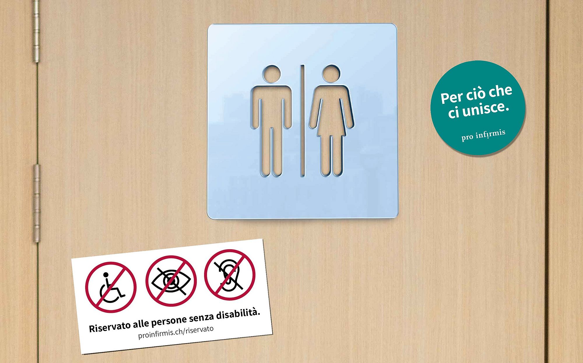 La porta di un bagno con il simbolo che rappresenta l'uomo e la donna. A titolo esemplificativo, in basso a sinistra è apposto l'adesivo con la scritta «riservato per persone senza disabilità». In alto a destra, l'adesivo con il messaggio «Per ciò che ci unisce».