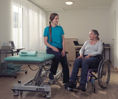 Une physiothérapeute et sa cliente en fauteuil roulant se regardent.