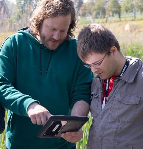 Drei junge Männer auf einer Wiese schauen in ein Computer-Tablet