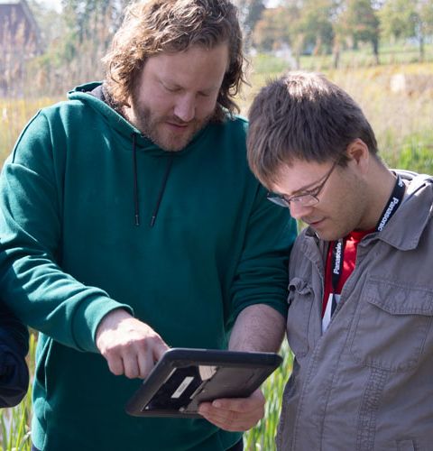 Drei junge Männer auf einer Wiese schauen in ein Computer-Tablet