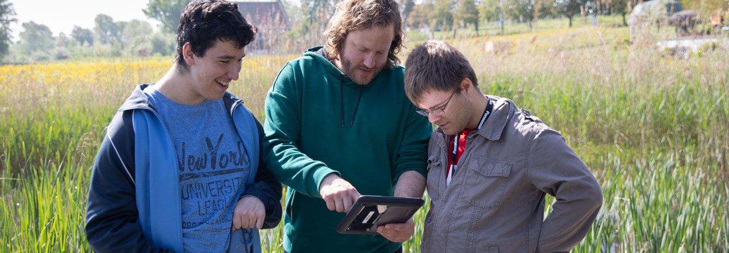 Drei junge Männer auf einer Wiese schauen in ein Computer-Tablet