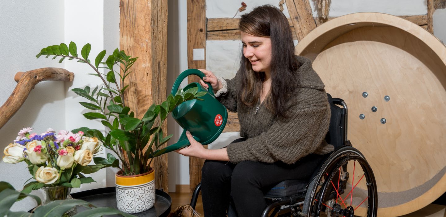 Une femme en fauteuil roulant arrose les plantes dans son appartement.