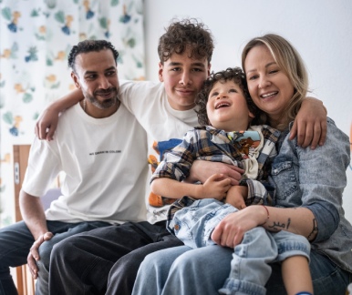 Józef sitzt lachend auf dem Schoss seiner Mutter. Sein Vater und sein älterer Bruder sitzen neben ihnen.