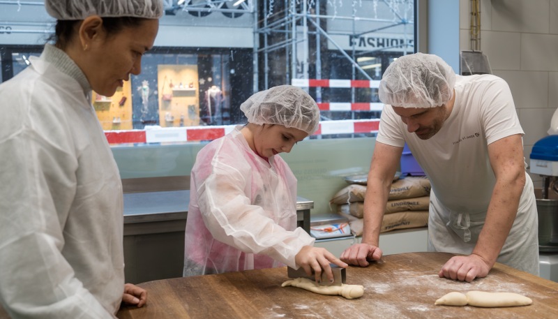 Un boulanger confectionne des bonshommes de Saint-Nicolas avec un enfant et une femme.