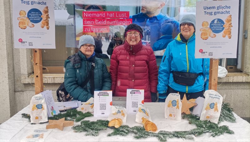 Drei Personen stehen hinter einem Stand mit inklusiven Grittibänzen auf dem Weihnachtsmarkt in St. Gallen.