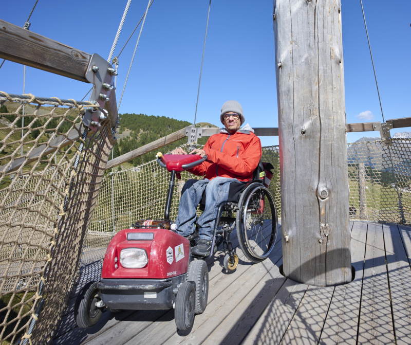 Eine Person im Rollstuhl auf einer Aussichtsplattform in den Bergen