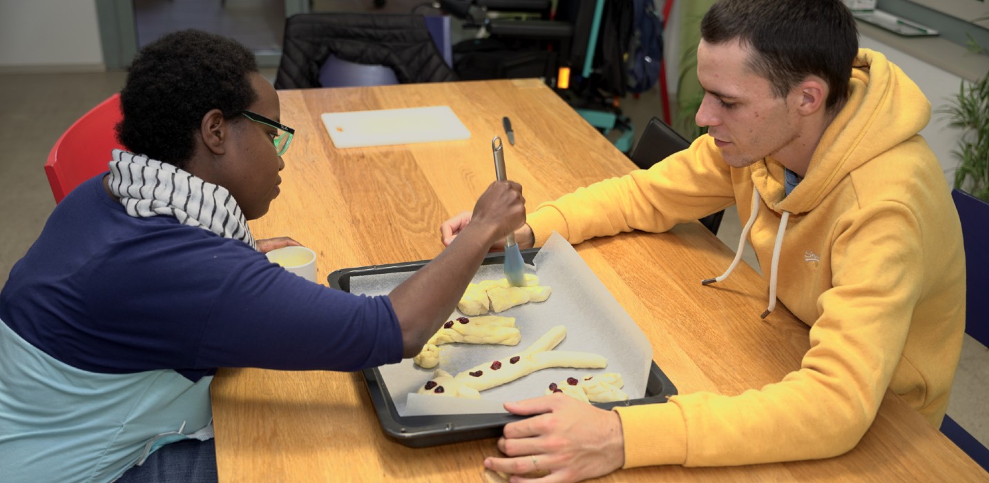 Deux jeunes hommes assis à une table badigeonnent des bonshommes de Saint-Nicolas.