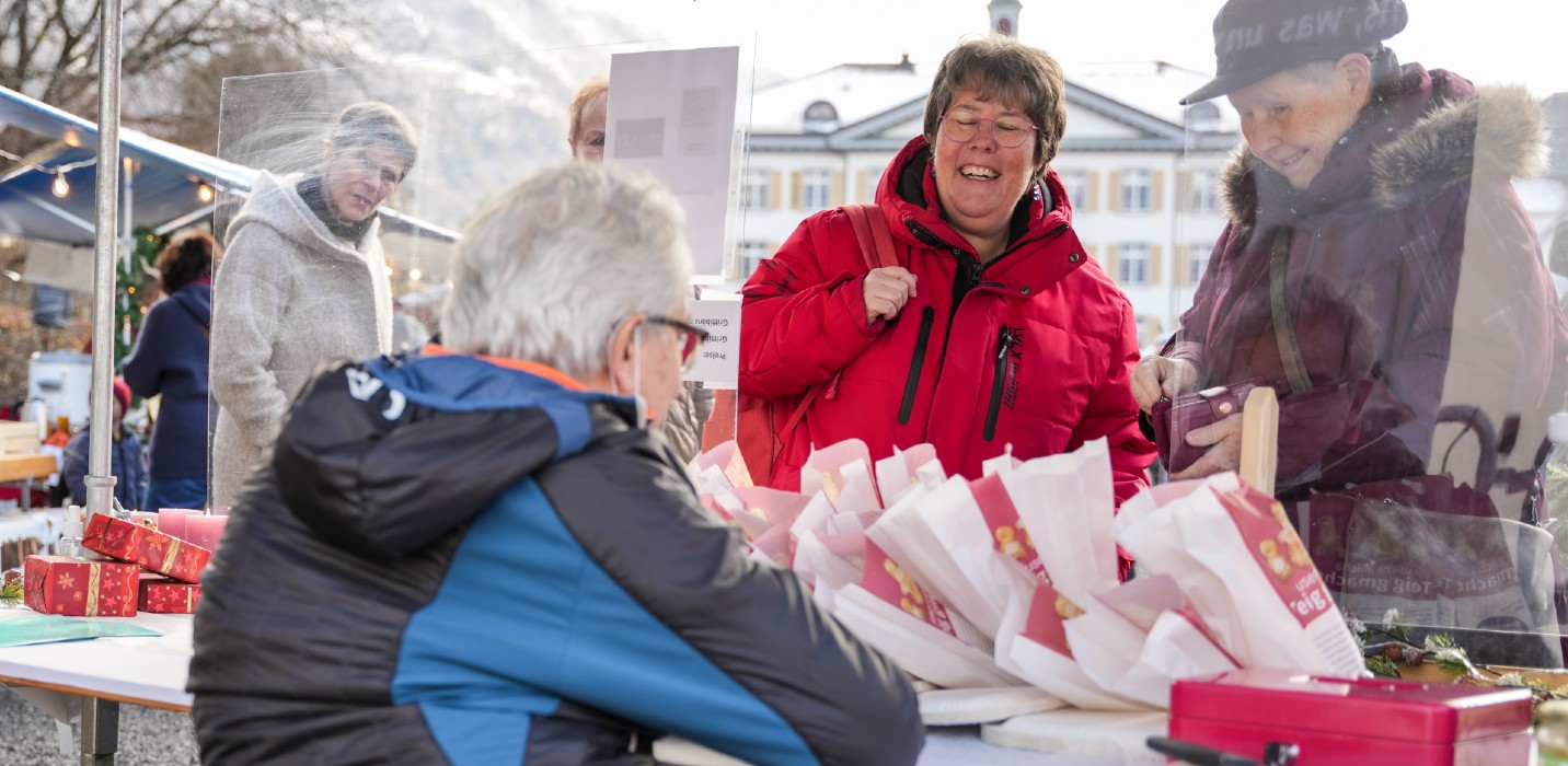 Mann (im Rollstuhl) am Stand verkauft einen Grittibänz an lachende Passantinnen.