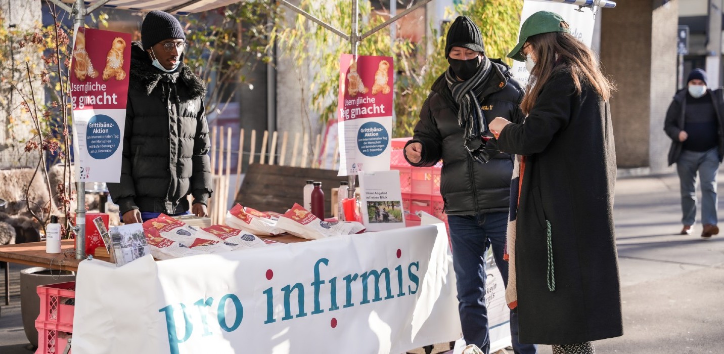 Pro-Infirmis-Stand, eine Frau kauft einen Grittibänz.