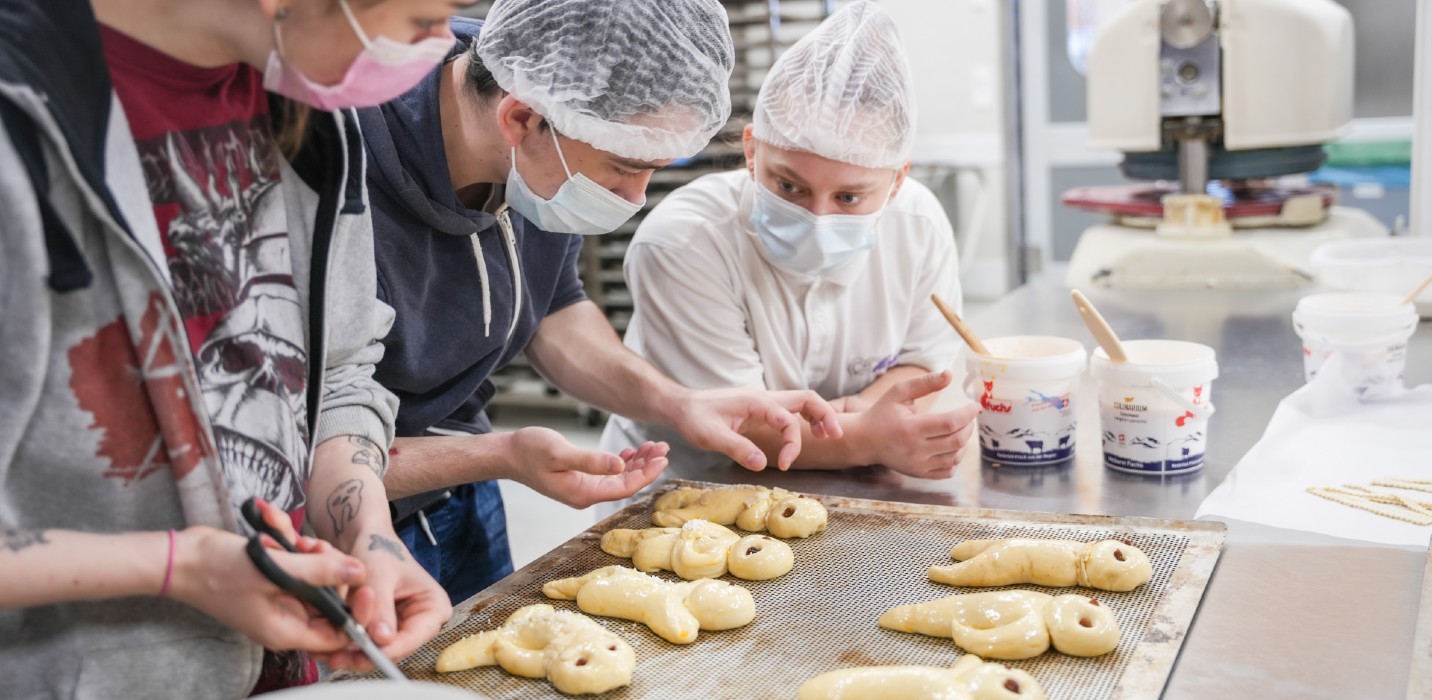 Trois jeunes confectionnent des bonshommes de Saint-Nicolas dans une boulangerie.
