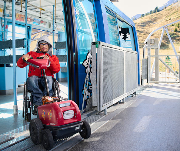 Un homme en fauteuil roulant équipé d’un dispositif de traction sort du téléphérique.