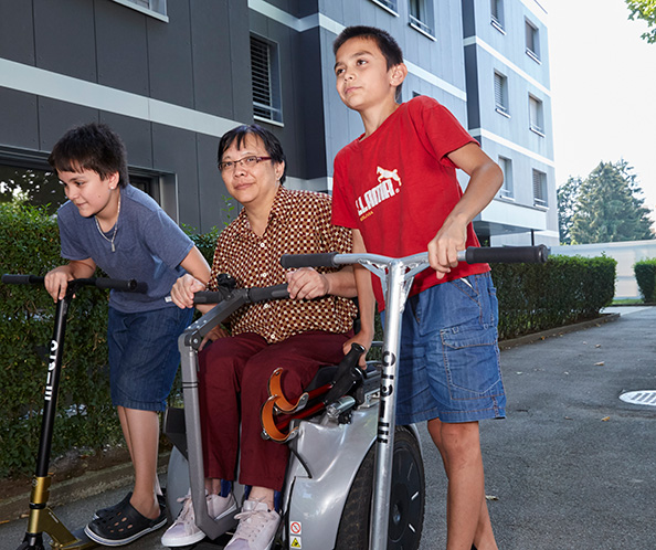 Mutter im elektrischen Rollstuhl, begleitet von ihren Söhnen auf Kickboards
