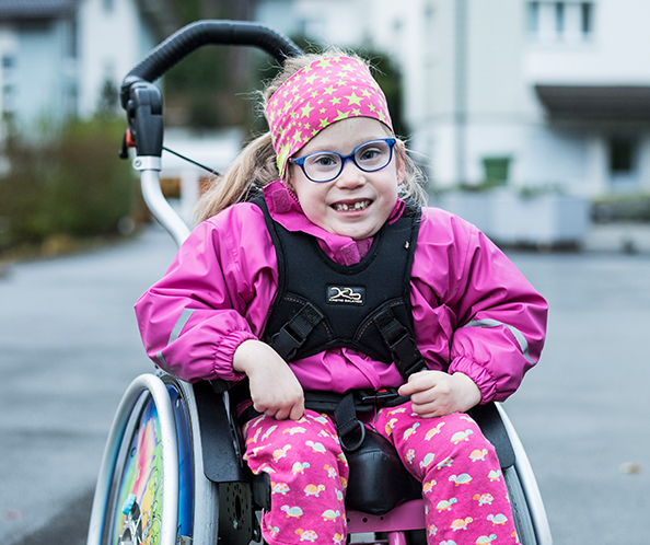 Bambina di sei anni paraplegica a causa della spina bifida seduta su una sedia a rotelle.