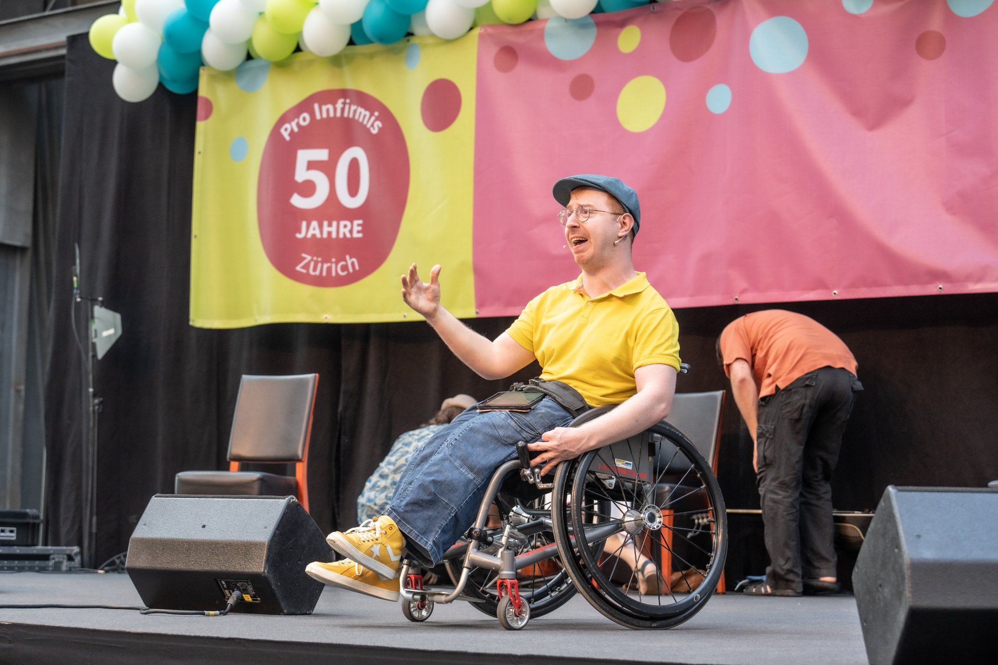 Jahn Graf (Mann im Rollstuhl) mit Headset auf der Bühne